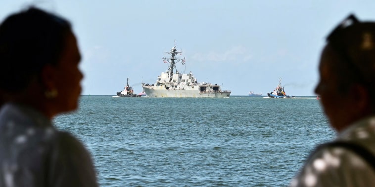 People watch the USS Gravely, a US Navy warship, departing the Port of Port of Spain.