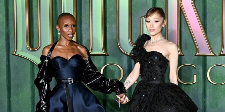 Cynthia Erivo, left, and Ariana Grande pose together in front of a green wall with text that reads "Wicked For Good"