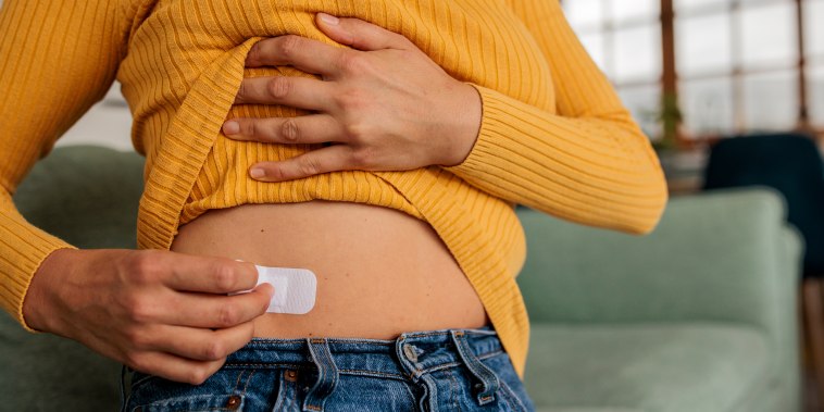 Unrecognizable woman in the comfort of her home applies a hormone replacement therapy patch to her waist.