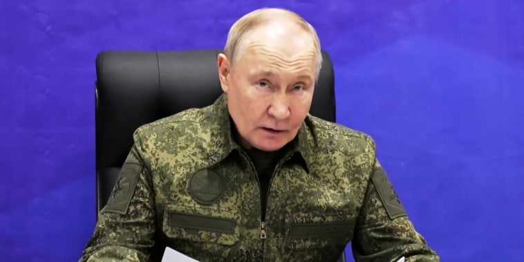 Russian President Vladimir Putin sat holding a papers against a purple background