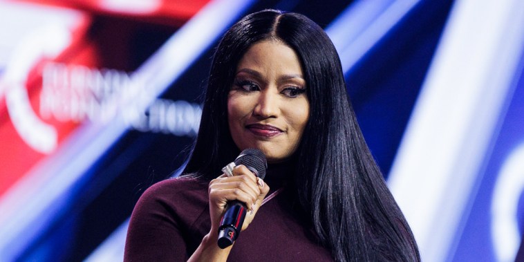 Nicki Minaj sits on a chair onstage holding a microphone