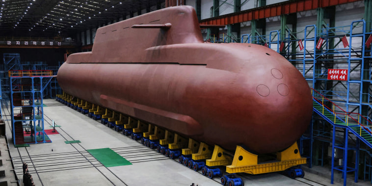 A large submarine is seen inside of a building as people look on