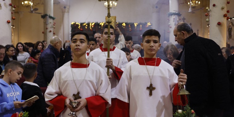 Alter servers and the cross bearer walk down the aisle during a Christmas mass celebrated with displaced worshippers at the Roman Catholic Church of the Holy Family in Gaza City.