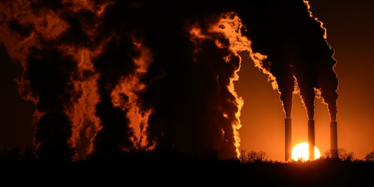 Silhouettes of large billowing smoke coming out of smoke stacks as the sun sets