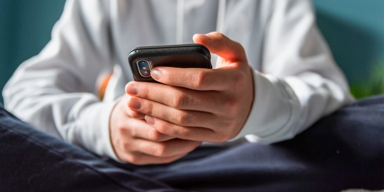 Close up of hands of teen boy in white sweater texting on phone.