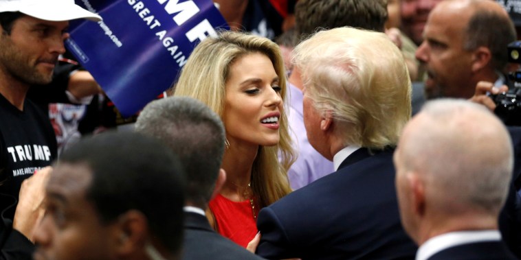 Carie Prejean smiles as she hugs Donald Trump. They are surrounded by a crowd of people