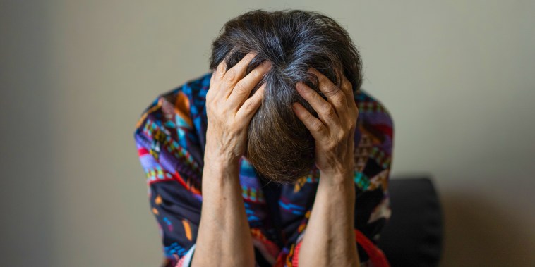 An old woman holding her head with both hands and slumped down