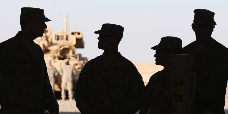 Four soldiers are silhouetted by bright desert sunlight. 
