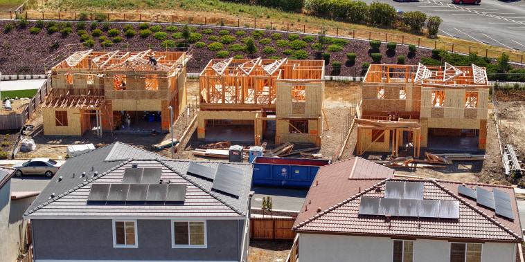 Three partially-built houses stand behind two finished houses with solar panels.