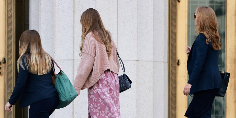 Three women are seen in profile view as they ascend the stone steps to a courthouse.