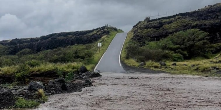 A view of flood waters in the front of a hilly road and grassy planes