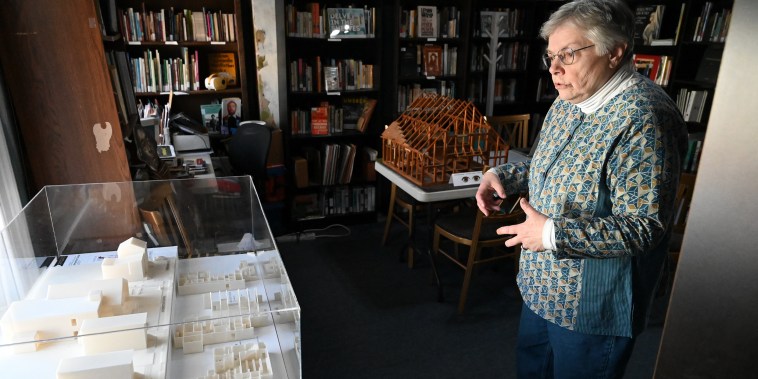 A woman stands in front of an architectural model encased in glass.