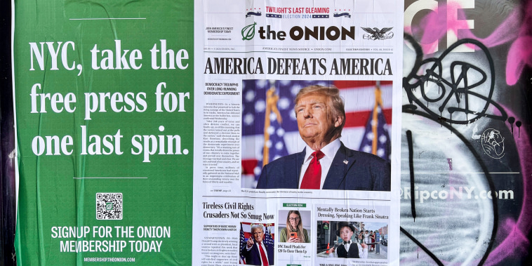 A poster for the Onion is pasted to a wall on a building, it reads "NYC, take the free press for one last spin." next to a fake newspaper article headlined "America defeats America" on top of a photo of Donald Trump
