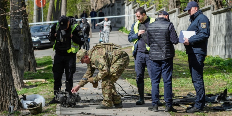 Police officers inspect fragments of a Russian drone on a sidewalk outside
