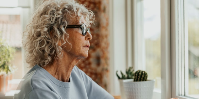 Thoughtful senior woman holding coffee cup while looking through window at home