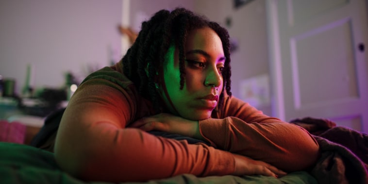 Thoughtful sad non-binary person lying on bed at home