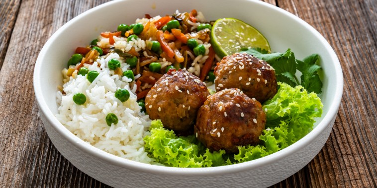 Meatballs in bowl served with white rice, stir-fried vegetables and peas on wooden background