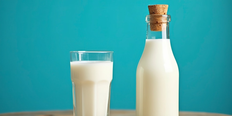 A glass bottle and a glass of creamy white liquid,Possibly milk or a milk-based beverage,Against a bright blue background