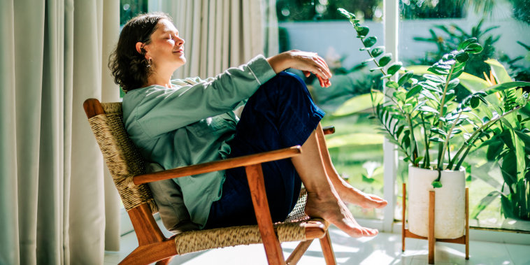 Woman relaxing in armchair by window enjoying morning sun