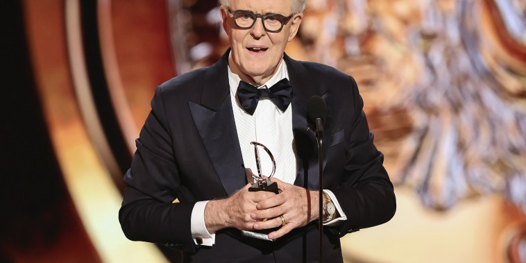 John Lithgow holding an Emmy, dressed in a tuxedo.
