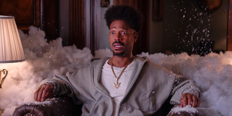 Marlon Wayans sits on a couch in a living room surrounded by foam with tears streaming down his face