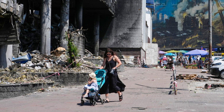 A mother pushes a stroller past a damaged building.