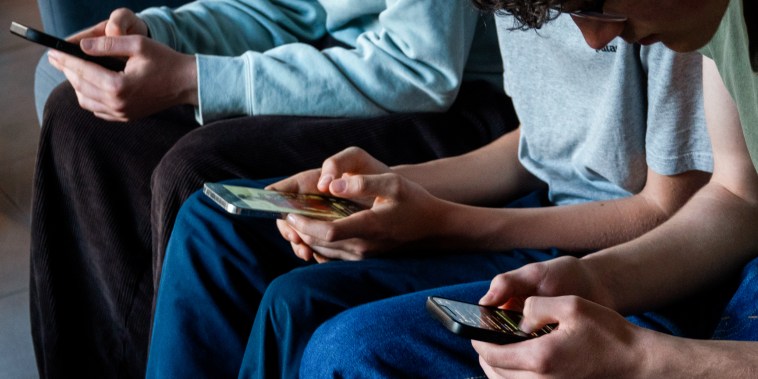 Three teenagers look at their smartphone screens on April 11, 2026.