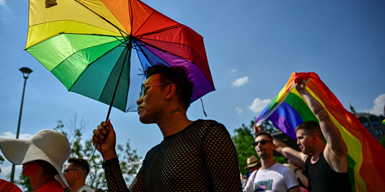 A person holds an umbrella in the colors of a Pride flag.