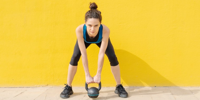 Young woman exercising with dumbbell in front of a yellow wall