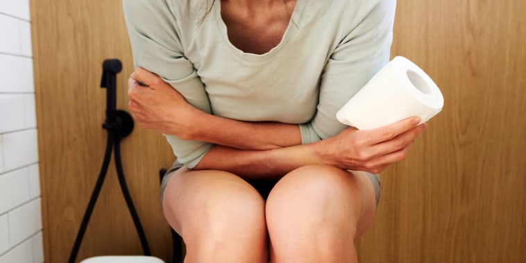 Image: Unrecognizable woman suffering from stomach ache while sitting on toilet in bathroom