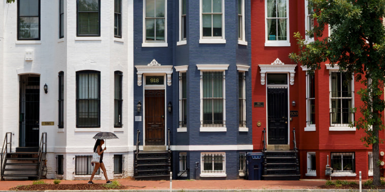 A woman with an umbrella walks past red, white and blue painted row houses.
