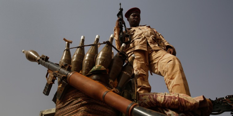 A Sudanese soldier from the Rapid Support Forces stands on a vehicle while holding a weapon.