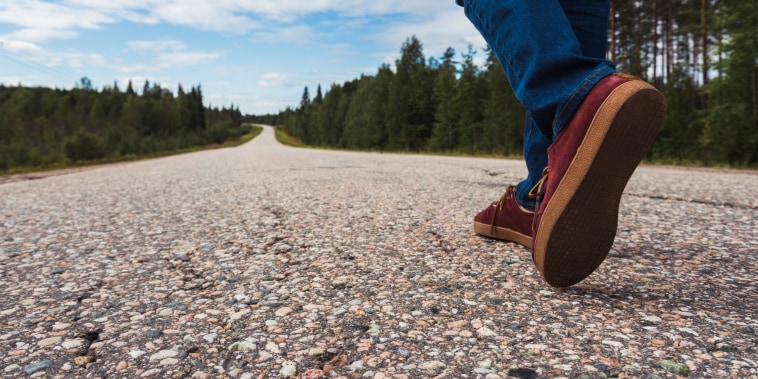 Finland, Lapland, feet of man walking on empty country road