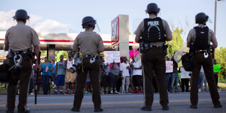 Image: Police officers watch as demonstrators protest the death of black teenager Michael Brown in Ferguson