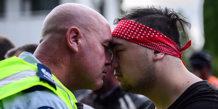 Image: A policeman and a biker gang member perform a hongi, a touching of noses, after a performance by different gang members of the haka as a tribute to victims in Christchurch