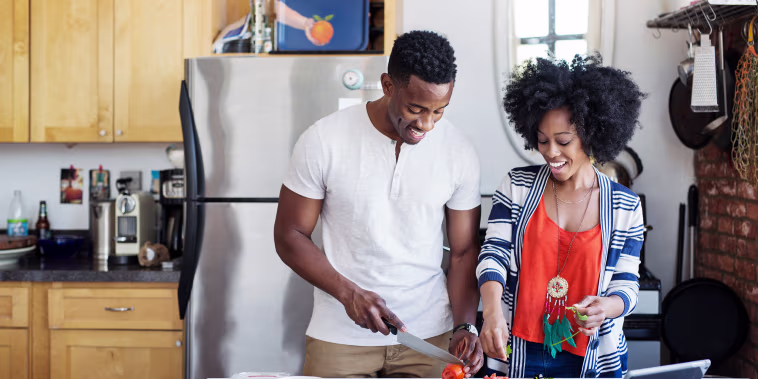 Happy man cutting tomatoes while standing with girlfriend at home