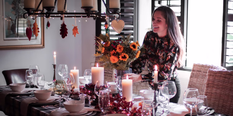 Smiling Mid Adult Woman Holding Arranging Flower Vase On Dinning Table At Home