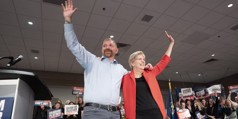 Elizabeth Warren and Graham Platner wave with their arms over each other's shoulders during a campaign event.
