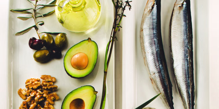 Still life of foods like olives, canola oil, mackerels, flaxseeds, avocado, and walnuts. 