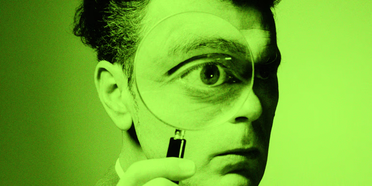 A man holding a magnifying glass to his eye.