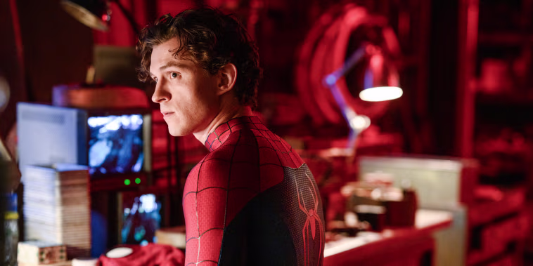 Tom Holland wearing a Spider Man suit and sitting at a work desk