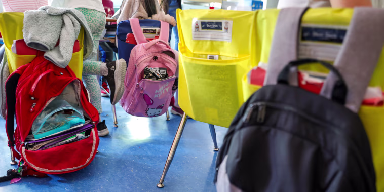 Student backpacks hang on the backs of classroom chairs.