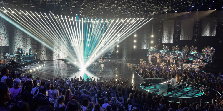 A wide view of the audience, judges, and a performer on stage during American Idol.