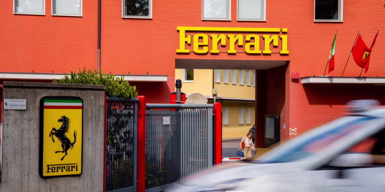 A detail view shows Ferrari factory signage, a yellow shield bearing the black prancing horse and Italian tricolor stripes, mounted on a concrete wall.