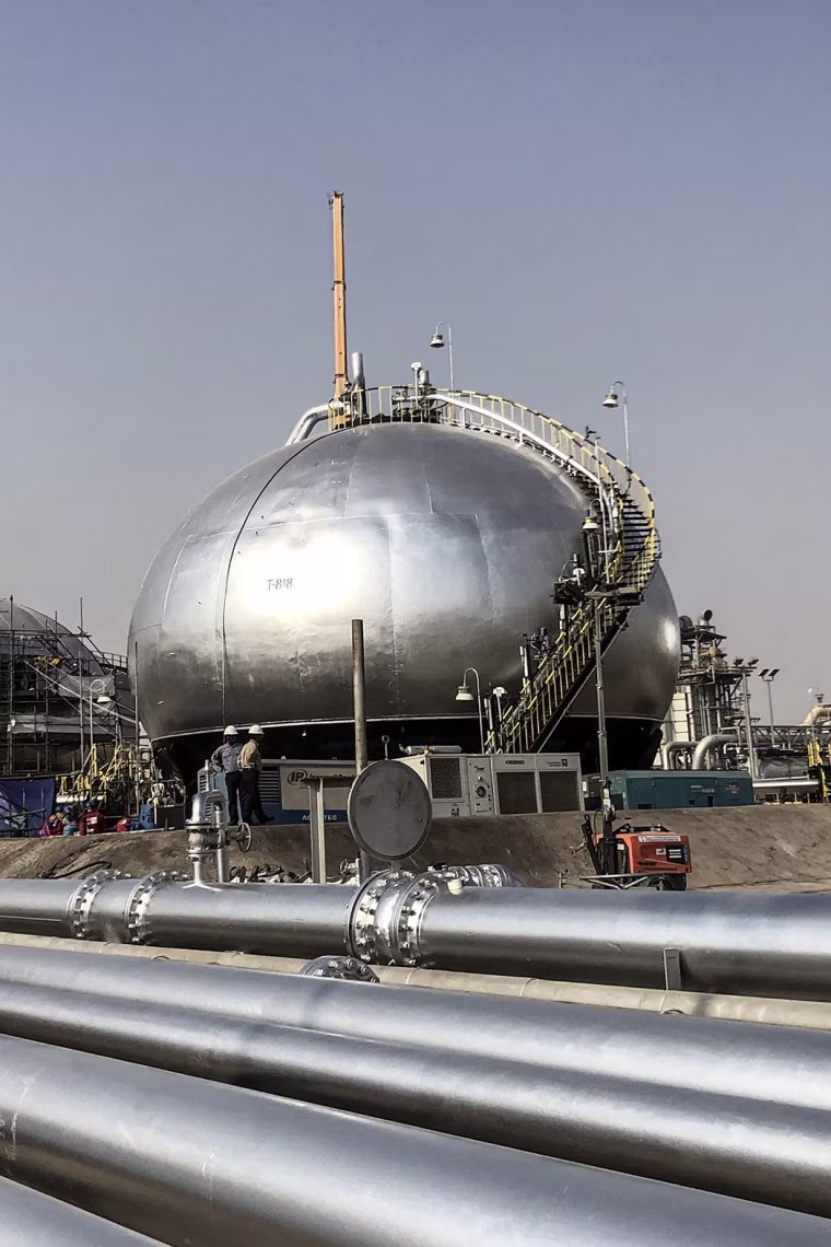 Round metallic storage tanks and pipelines in a desert landscape.