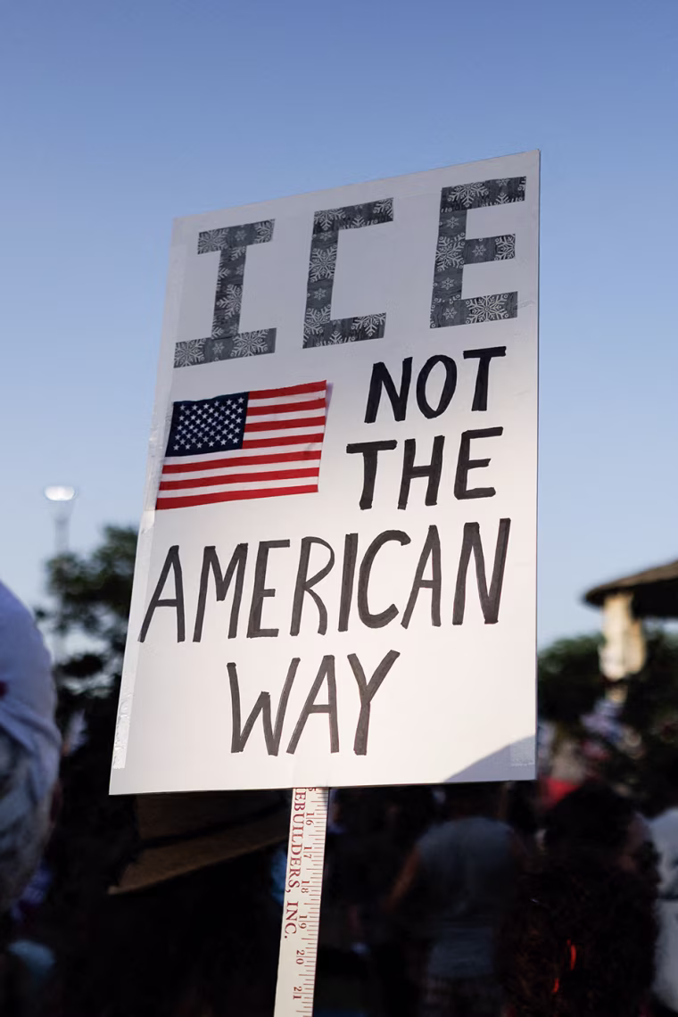 A man holds a sign reading ICE NOT THE AMERICAN WAY.