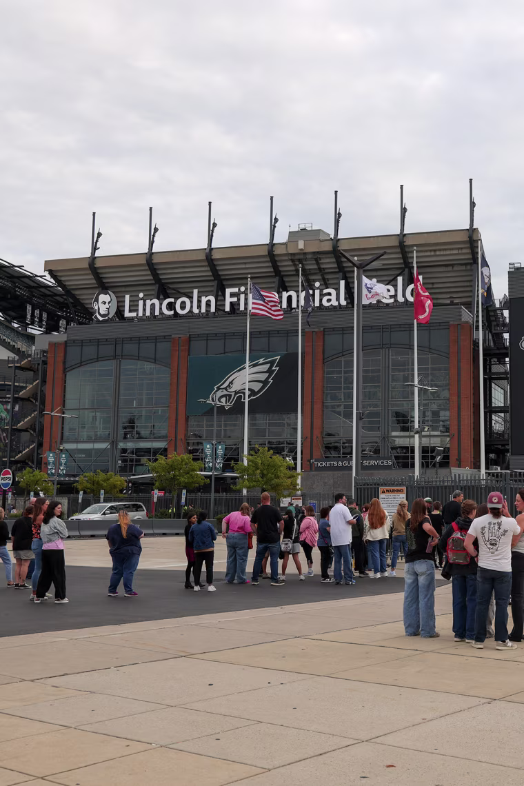 People congregating outside a large outdoor sports venue.