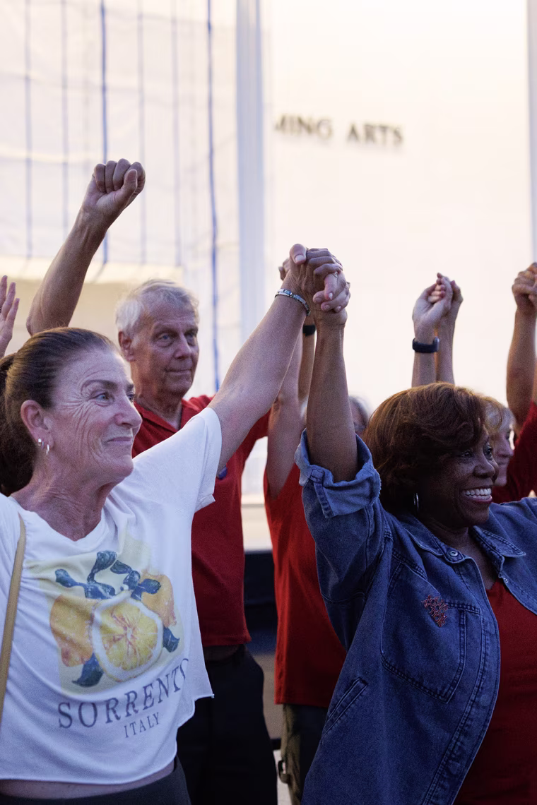 People joining hands in front of the white stone facade of the Kennedy Center.
