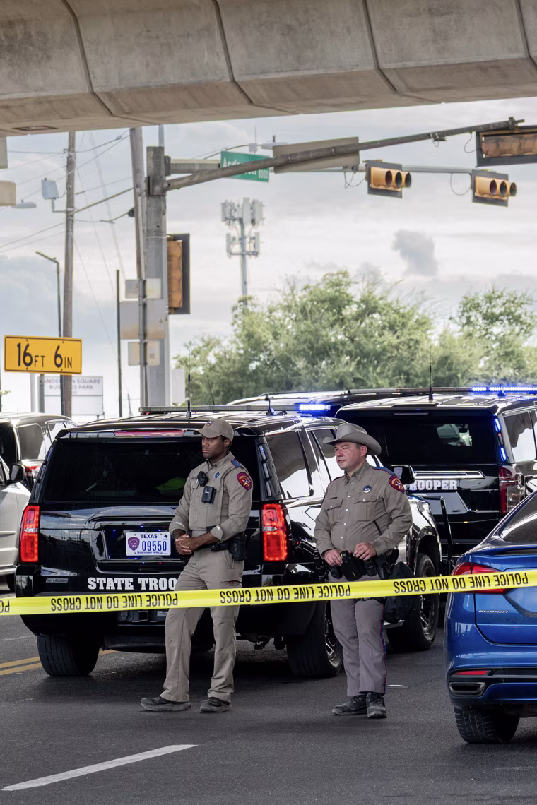 Two law enforcement agents standing behind police tape under an overpass.