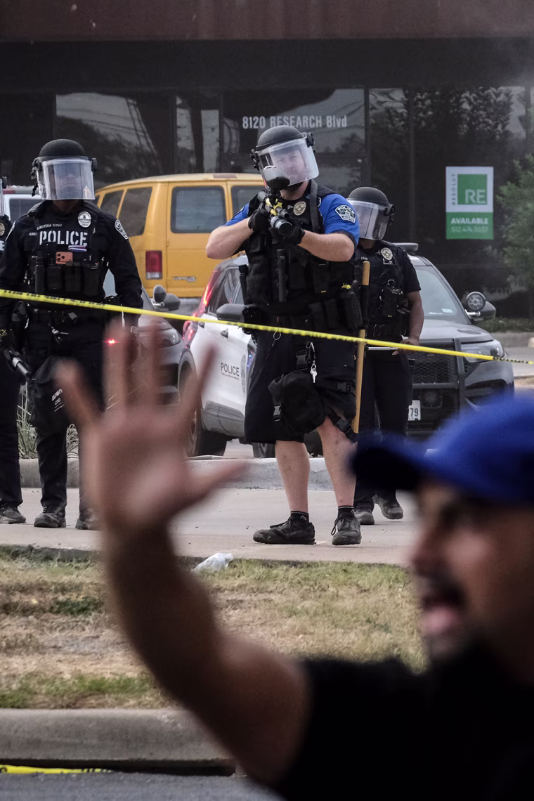 Police officers with non-lethal weapons in the background behind a protester. 